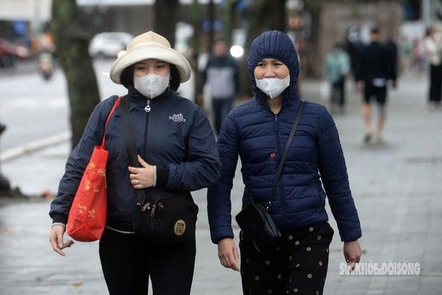 Hai người phụ nữ mặc áo ấm và khẩu trang đi bộ trên đường phố Hà Nội trong đợt rét đậm