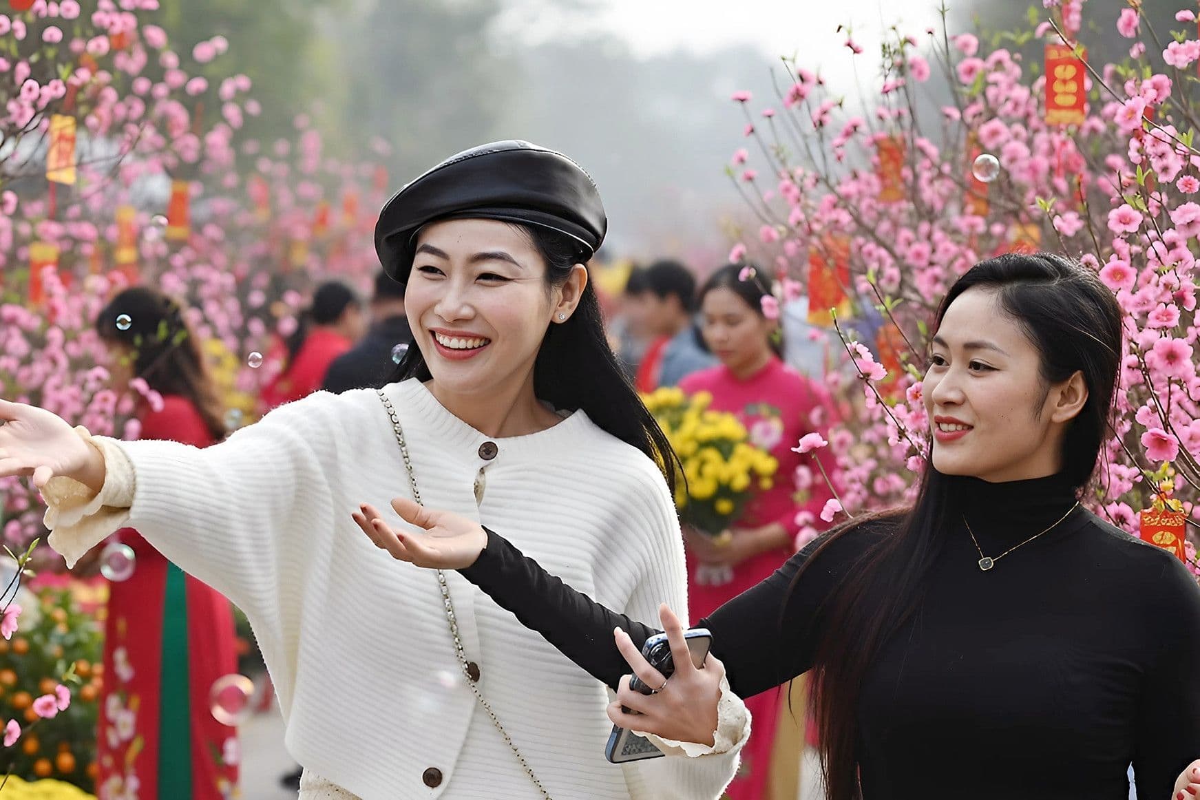 Hai người phụ nữ tươi cười giữa vườn hoa đào nở rộ, tượng trưng cho niềm vui và sự đặc biệt của hiện tượng Lưỡng Lập Xuân.