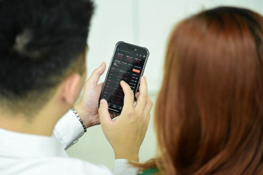 Hai nhà đầu tư đang xem bảng giá chứng khoán trên điện thoại di động với nhiều mã giảm điểm, thể hiện thị trường đang biến động tiêu cực.