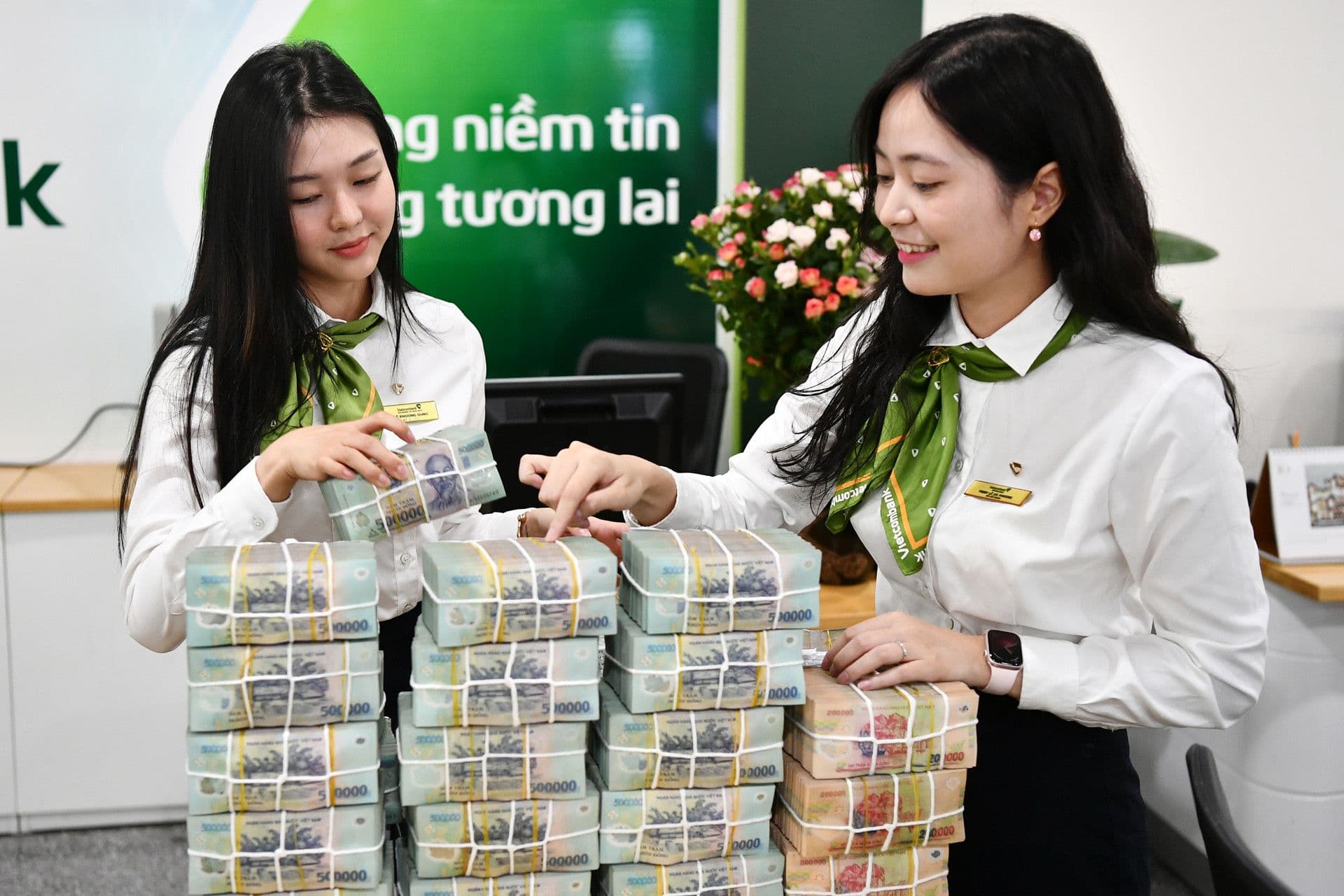 Hai nhân viên ngân hàng đang sắp xếp các cọc tiền đồng Việt Nam, tượng trưng cho dòng chảy vốn và lãi suất trong nền kinh tế.