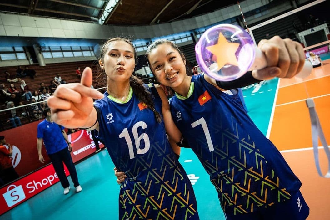 Hai vận động viên bóng chuyền nữ U21 Việt Nam tươi cười tạo dáng trên sân.