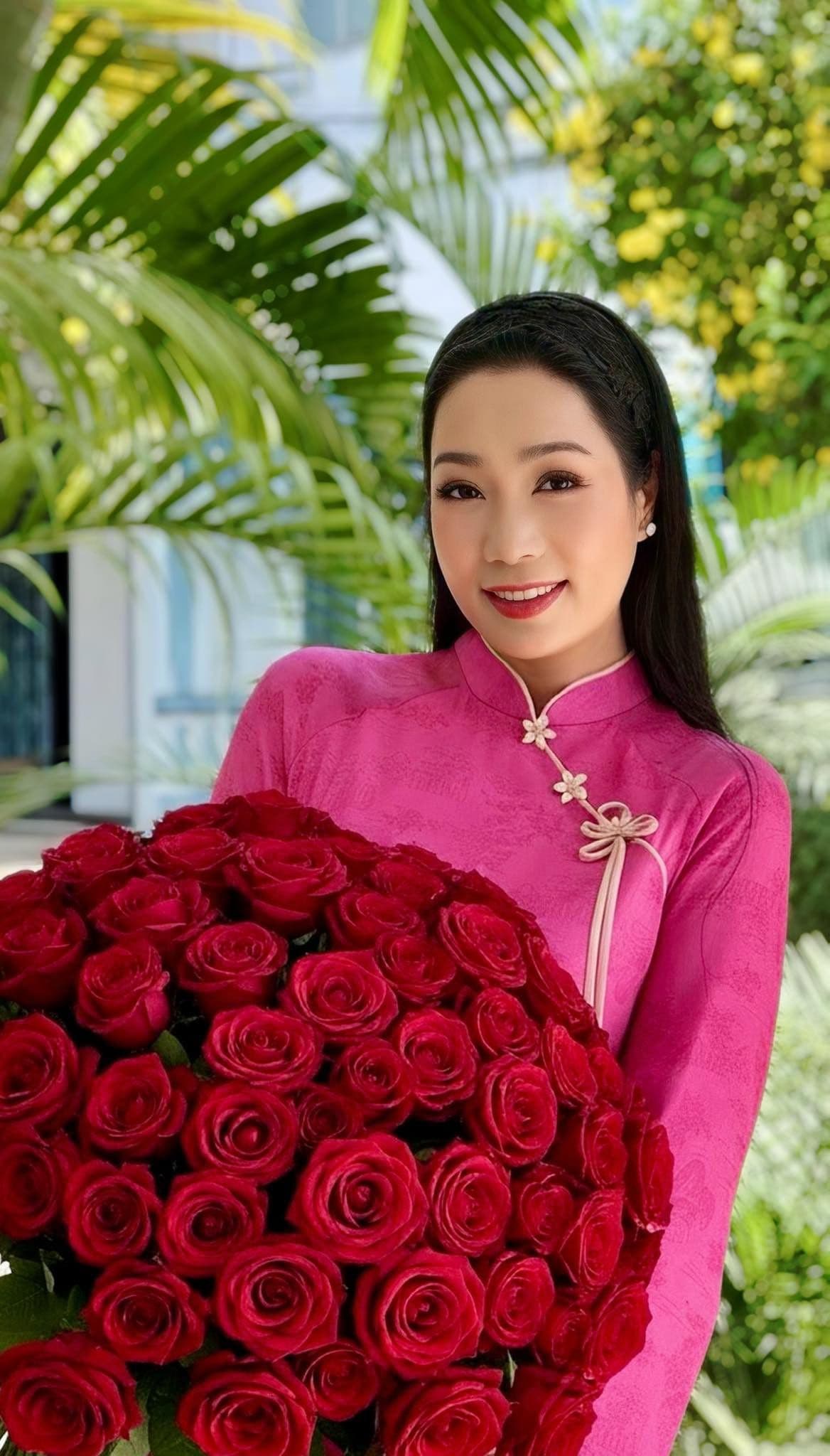 Hari Won rạng rỡ trong tà áo dài hồng, ôm bó hoa hồng đỏ, thể hiện sự chân thật và niềm vui của cô.