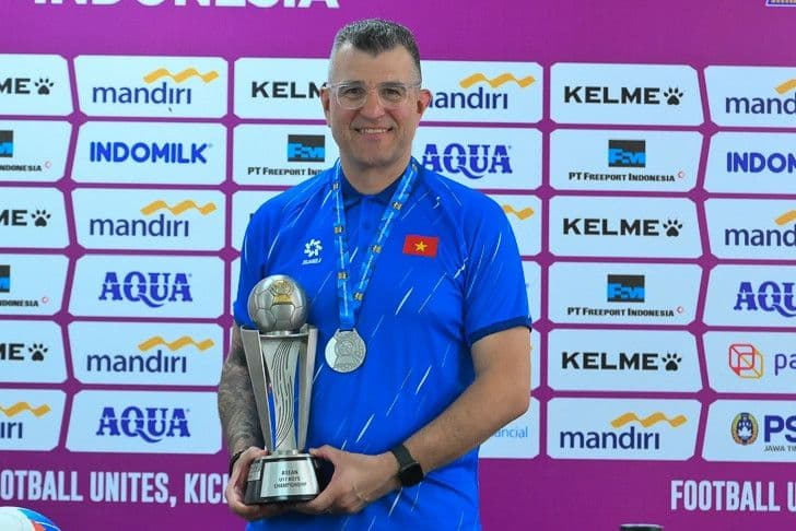 HLV Cristiano Roland của U17 Việt Nam mỉm cười với cúp vô địch, tượng trưng cho triết lý phát triển bóng đá bền vững.