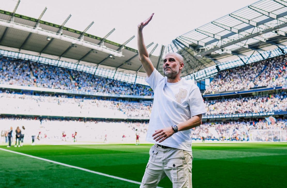 HLV Pep Guardiola vẫy tay chào người hâm mộ tại sân Etihad, trong không khí chuẩn bị cho buổi tiệc chia tay.