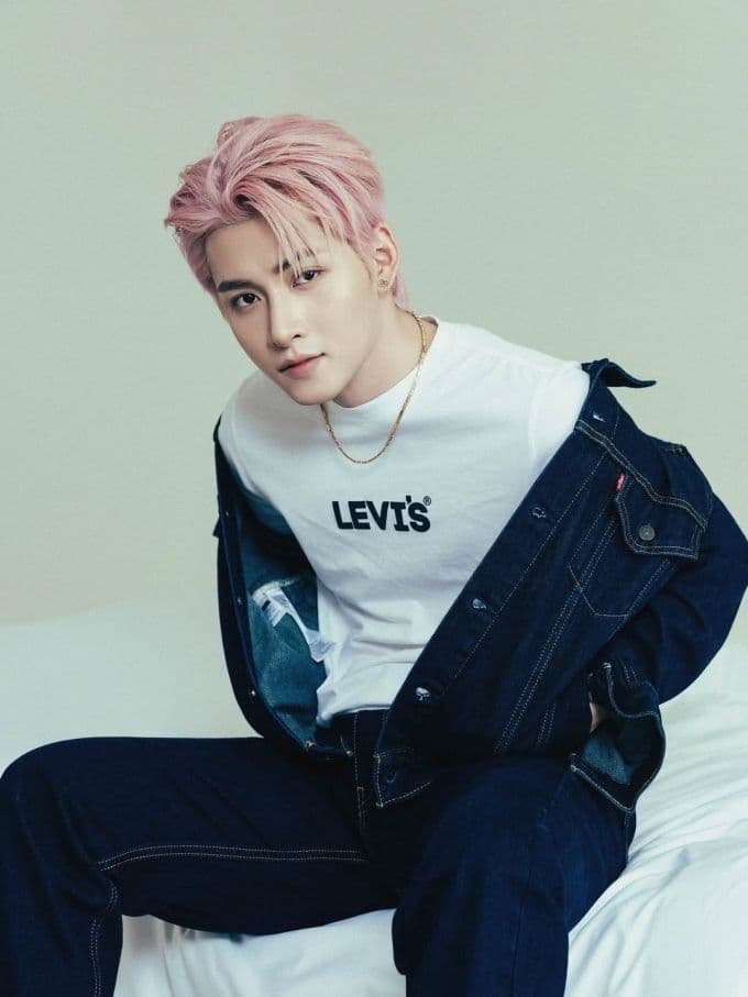 Hùng Huỳnh với mái tóc hồng, mặc áo phông Levi's và áo khoác denim, thể hiện phong cách trẻ trung và hiện đại.