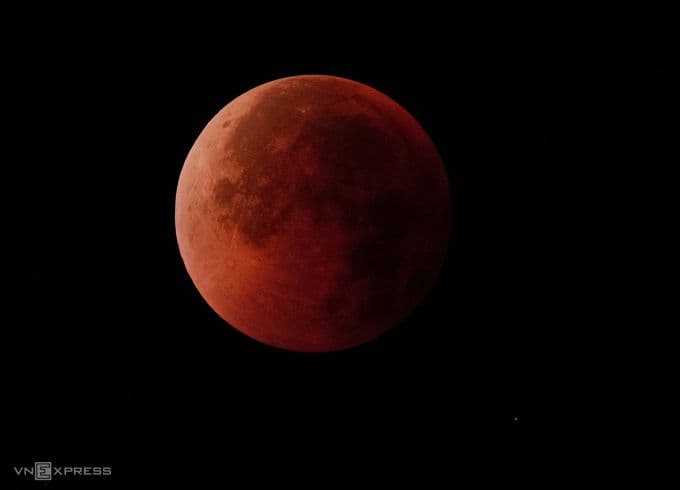 Hình ảnh cận cảnh Mặt Trăng trong pha nguyệt thực toàn phần, hiện lên với sắc đỏ cam rực rỡ trên nền trời đêm đen.