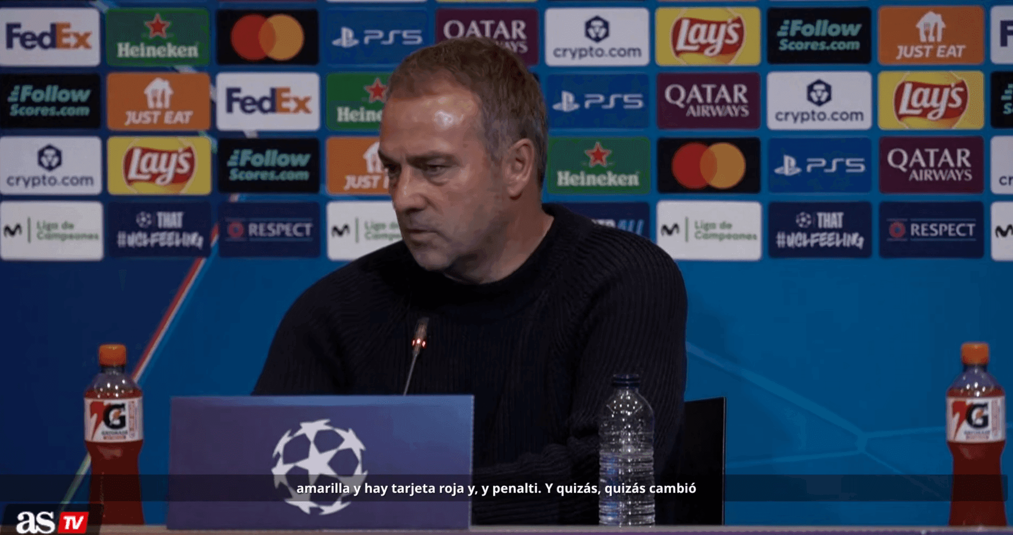 Huấn luyện viên tại buổi họp báo với nhiều logo nhà tài trợ và biểu tượng UEFA Champions League, thể hiện sự thương mại hóa của bóng đá.