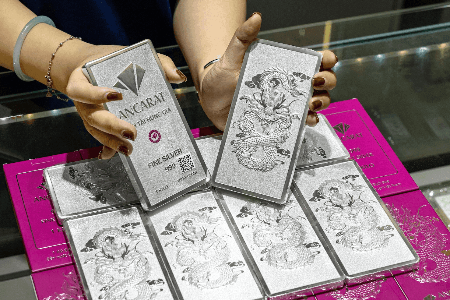 Đôi tay đang cầm hai thỏi bạc Ancarat 1kg, thể hiện kim loại quý đang đối mặt với biến động giá mạnh.