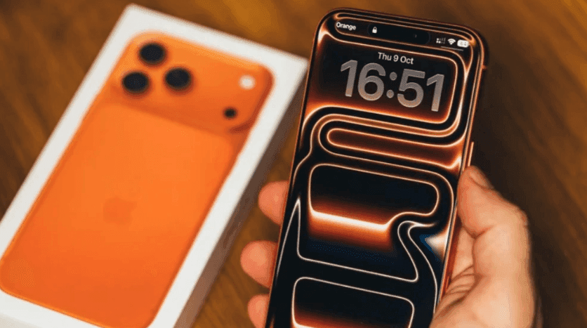 iPhone 18 Pro Max màu cam với màn hình hiển thị đồng hồ và họa tiết ánh sáng, cùng hộp sản phẩm.