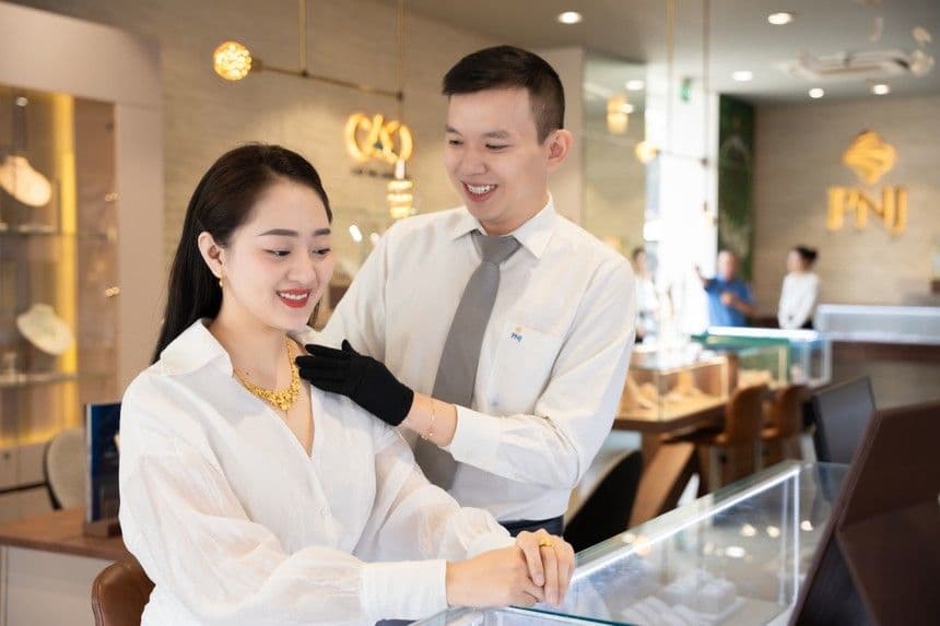 Khách hàng đang thử trang sức vàng tại cửa hàng PNJ với sự hỗ trợ của nhân viên, phản ánh hoạt động kinh doanh và trải nghiệm mua sắm trong ngành vàng bạc đá quý.
