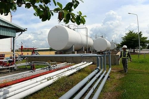 Khu vực bồn chứa xăng dầu với đường ống và một công nhân đang đi bộ, thể hiện nỗ lực đảm bảo nguồn cung năng lượng tại Việt Nam.