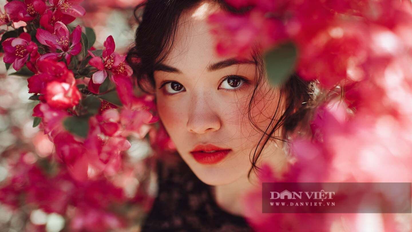Khuôn mặt người phụ nữ với ánh nhìn sâu sắc giữa những cánh hoa hồng, tượng trưng cho sự chiêm nghiệm về ý nghĩa của may mắn.
