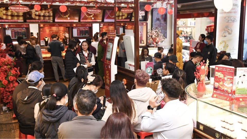 Khung cảnh đông đúc bên trong một cửa hàng vàng, với nhiều khách hàng đang giao dịch, thể hiện tâm lý đám đông và hoạt động sôi nổi của nhà đầu tư.
