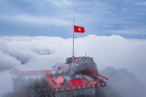Lá cờ Việt Nam tung bay trên đỉnh núi mây phủ, tượng trưng cho tinh thần chinh phục và vẻ đẹp hùng vĩ của những cung đèo lịch sử.