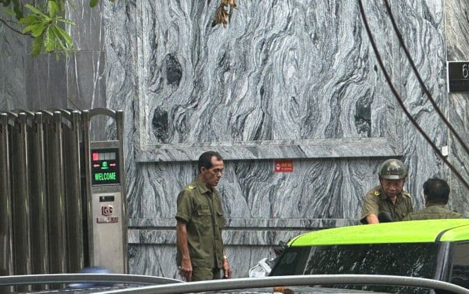 Lực lượng an ninh bên ngoài văn phòng PJICO trong cuộc khám xét của cảnh sát, thể hiện sự chấn động của vụ án.