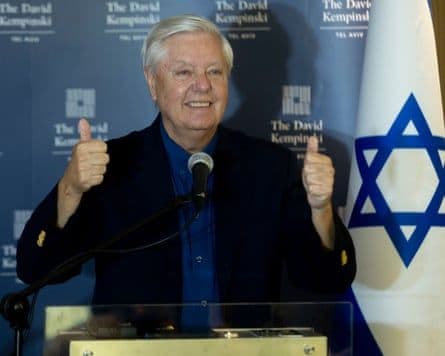 Lindsey Graham mỉm cười và giơ ngón tay cái bên cạnh lá cờ Israel