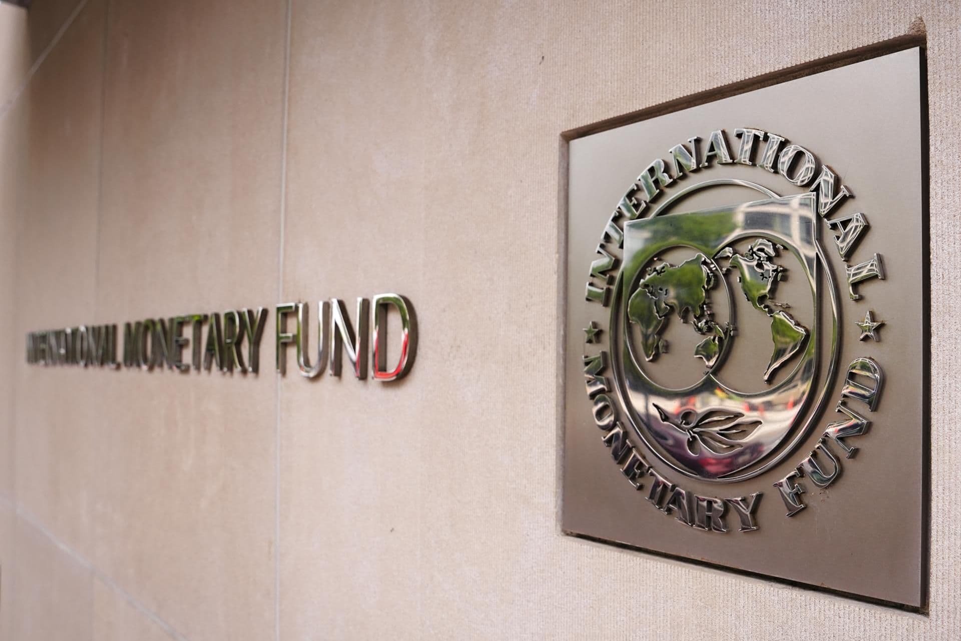 Logo Quỹ Tiền tệ Quốc tế (IMF) trên tường, tượng trưng cho báo cáo kinh tế toàn cầu và các rủi ro từ xung đột Trung Đông, đầu tư AI.