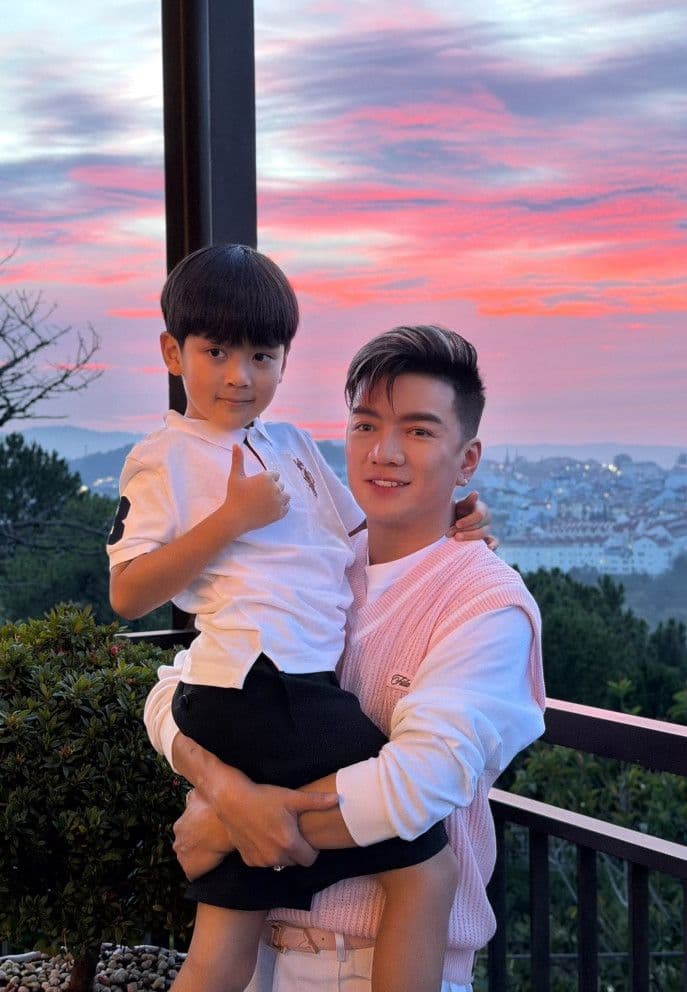 Đàm Vĩnh Hưng bế con trai Polo dưới ánh hoàng hôn, tượng trưng cho hạnh phúc gia đình và sự bình yên.