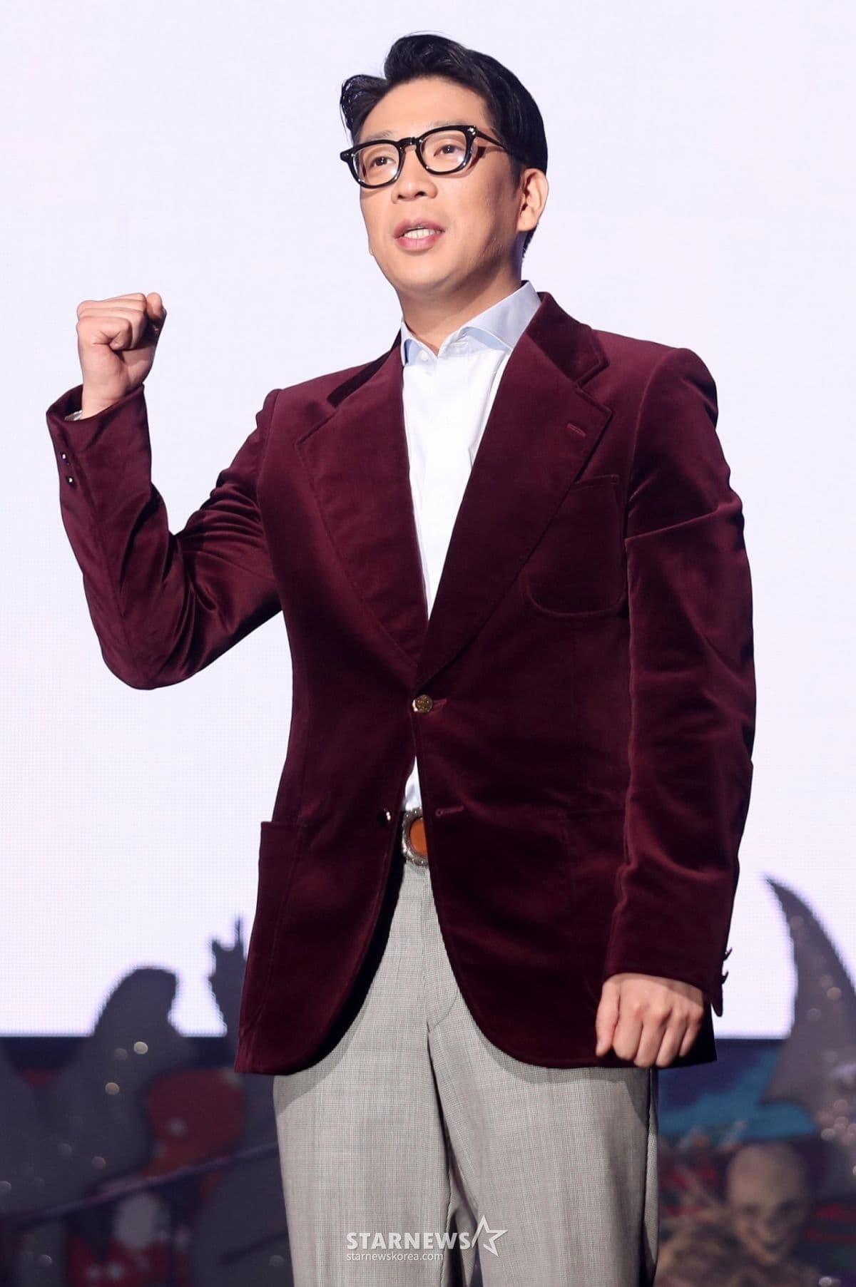 MC Mong đứng trên sân khấu, mặc áo khoác nhung và kính, giơ nắm đấm thể hiện sự quyết tâm trong cuộc chiến danh tiếng.