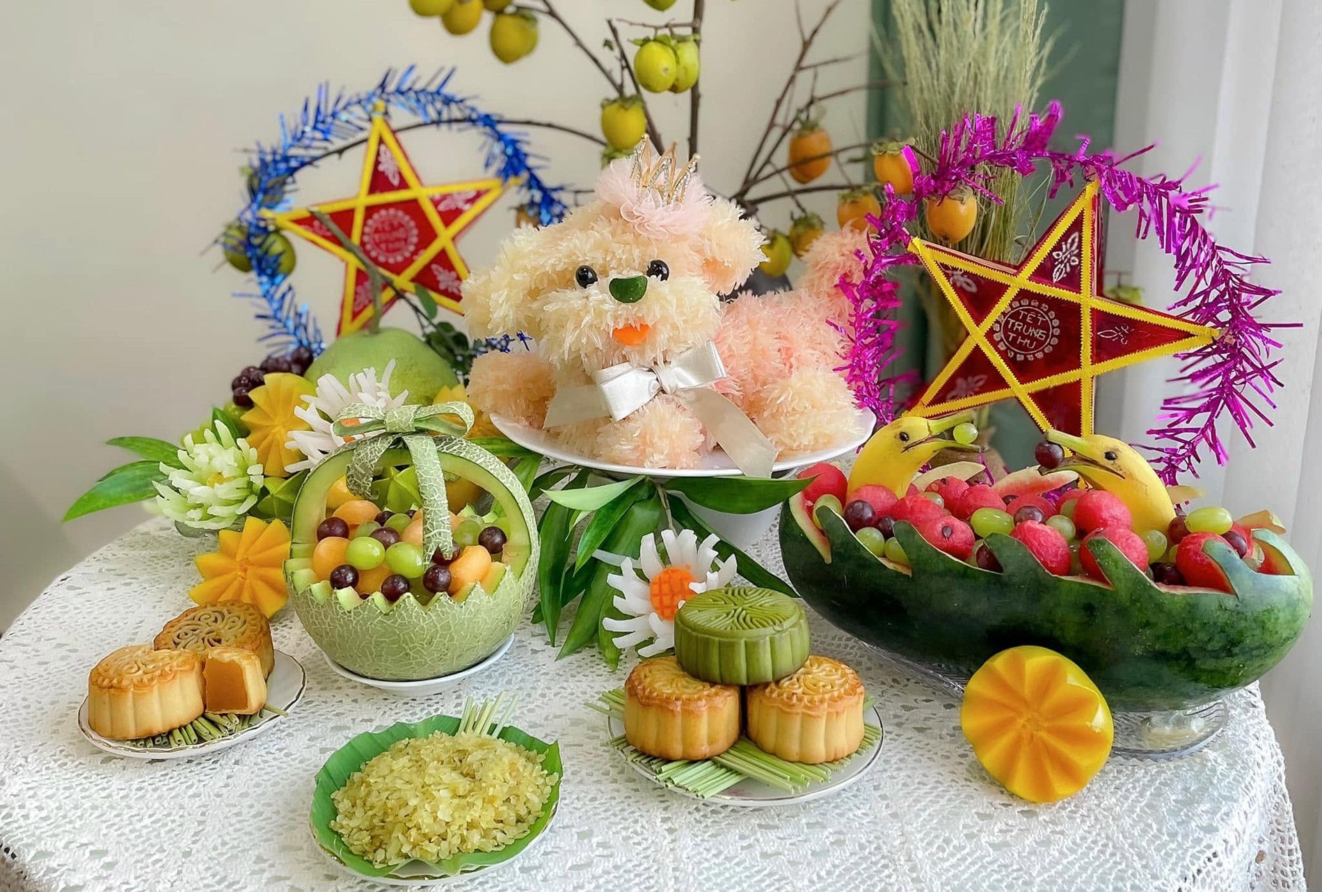 Mâm cỗ Trung Thu với bánh trung thu, hoa quả và đồ chơi hình chó, tượng trưng cho Tết Đoàn Viên và sự an yên trong gia đình.