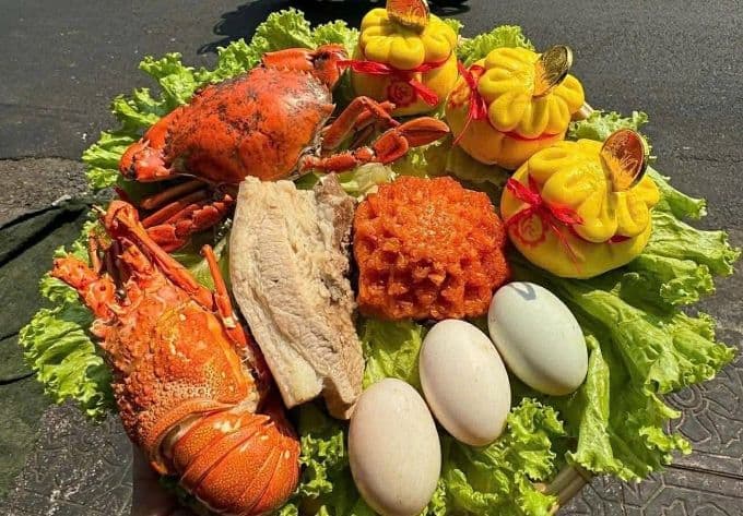 Mâm cúng Thần Tài với bộ Tam Sên gồm tôm hùm, cua, cá và trứng, cùng các lễ vật khác, thể hiện sự đầy đủ và sung túc.