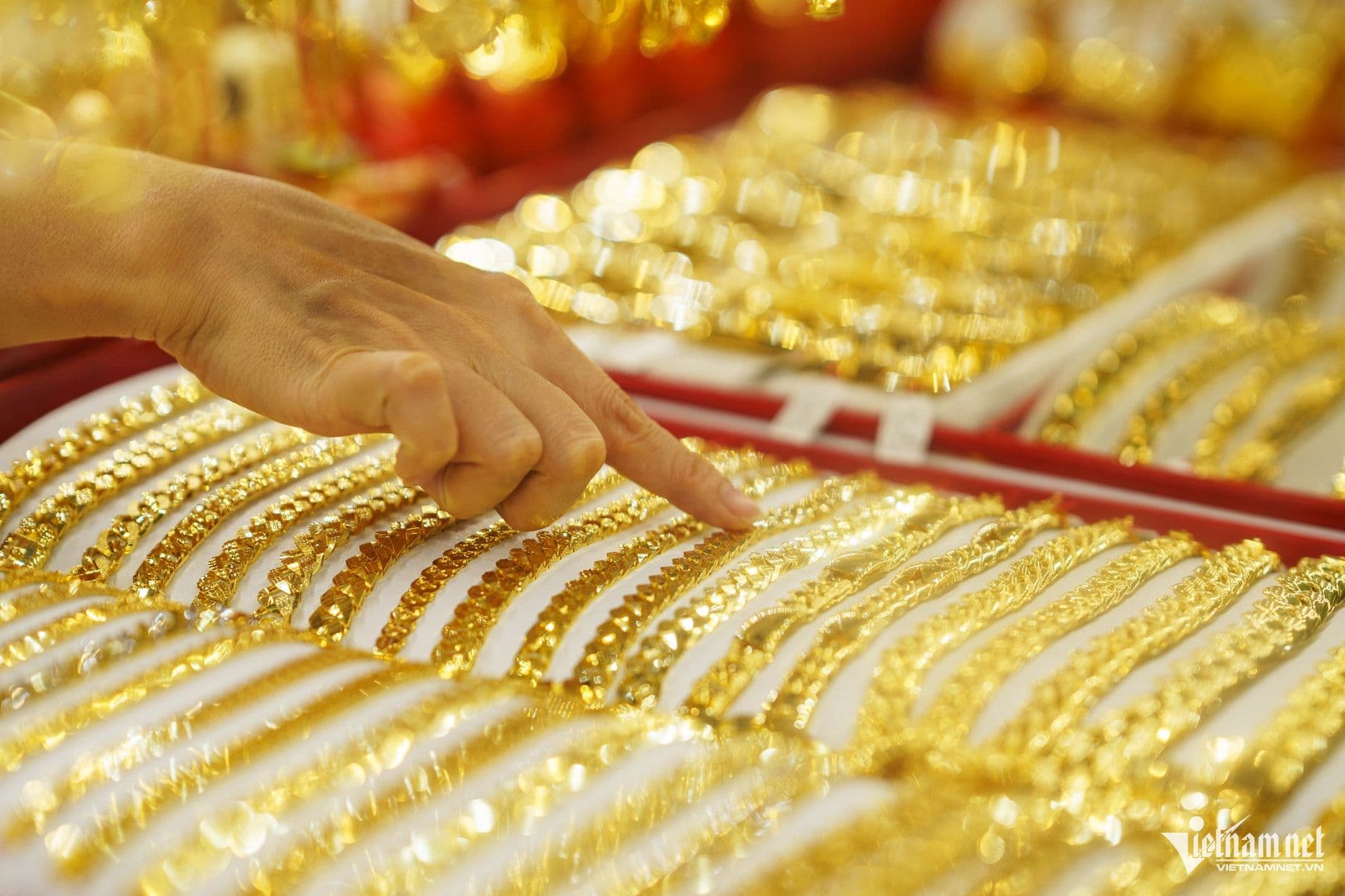 Một bàn tay đang chỉ vào những món đồ vàng SJC được trưng bày trong cửa hàng, thể hiện thị trường vàng sôi động.