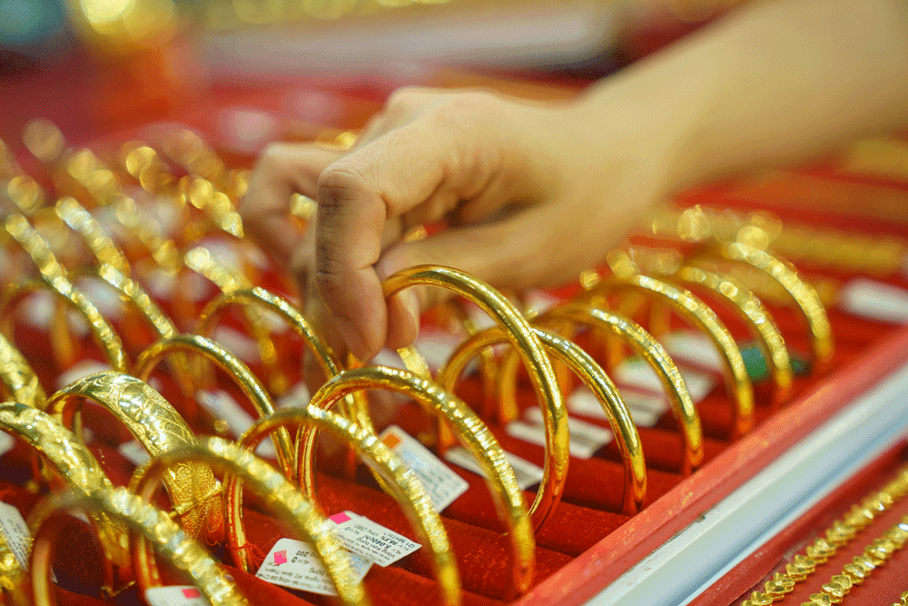 Một bàn tay đang chọn vòng vàng trong cửa hàng trang sức, tượng trưng cho thị trường vàng sôi động.