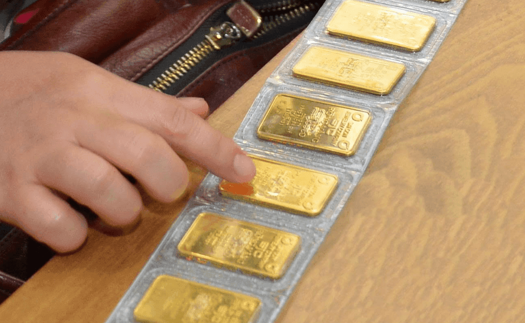 Một bàn tay chỉ vào các miếng vàng SJC được đóng gói, thể hiện giao dịch vàng miếng trong nước.