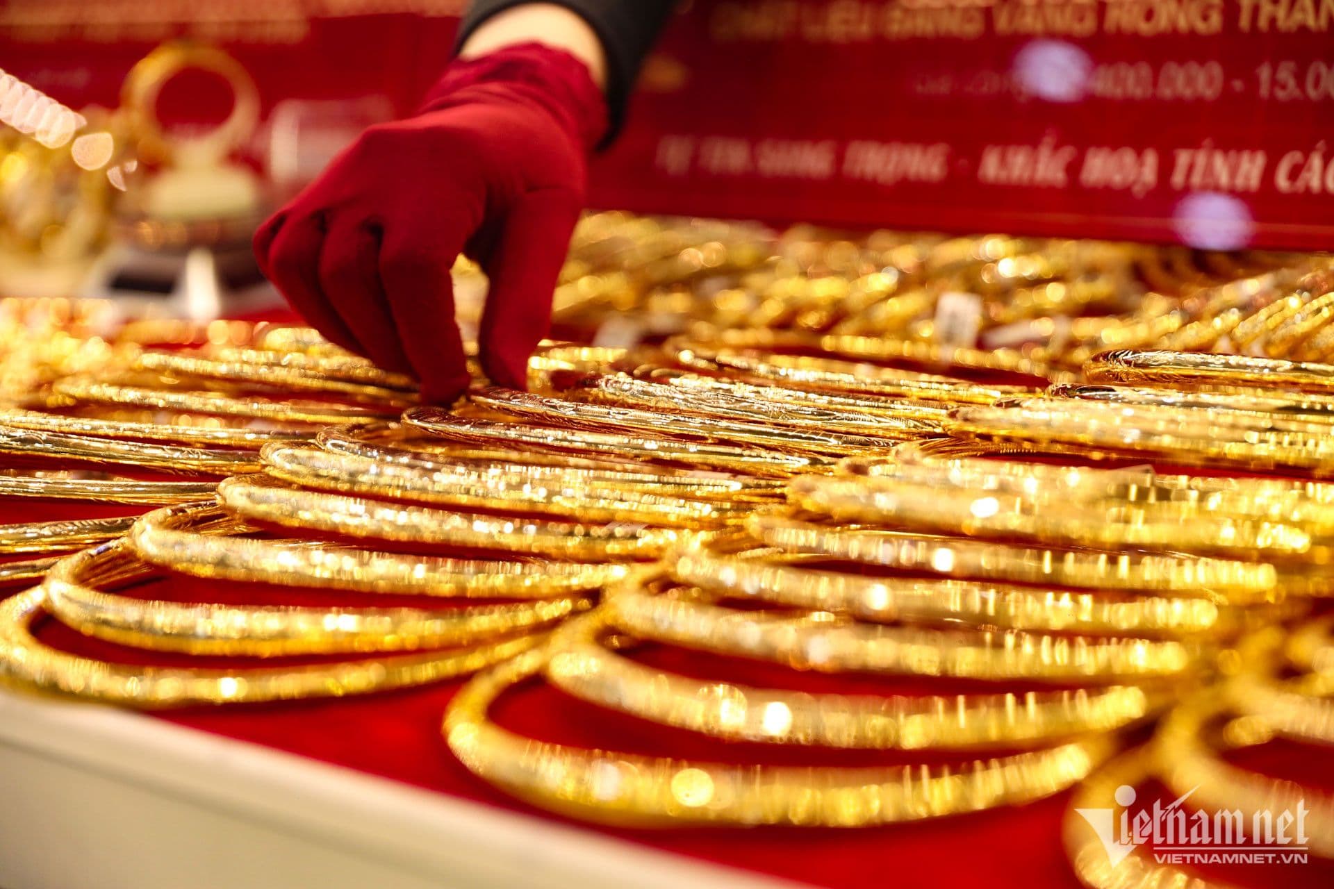 Một bàn tay đeo găng đỏ đang sắp xếp những chiếc vòng vàng trên khay, minh họa cho thị trường vàng trang sức và sự chênh lệch giá.