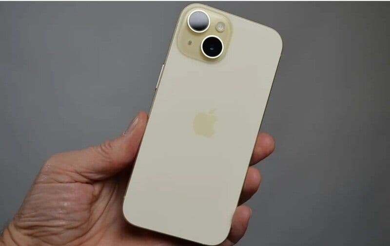 Một chiếc iPhone 15 màu trắng ngà được cầm trên tay, biểu tượng cho thương hiệu và hệ sinh thái Apple.