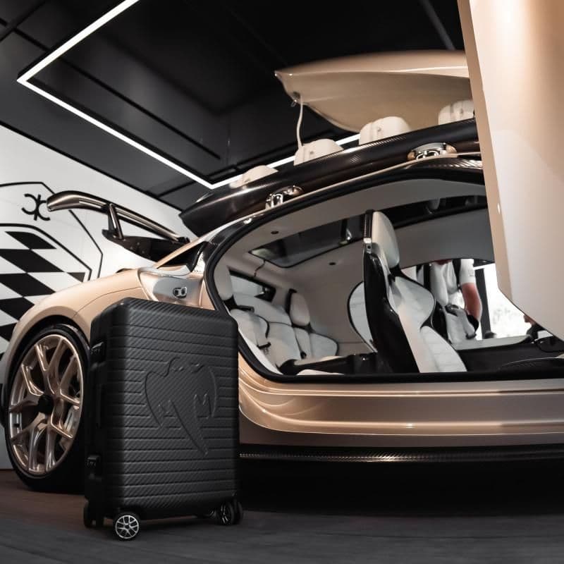 Một chiếc Koenigsegg Gemera màu vàng be với cửa mở và bộ hành lý sợi carbon độc quyền MON CARBONE, thể hiện sự kết hợp giữa kỹ thuật và nghệ thuật.