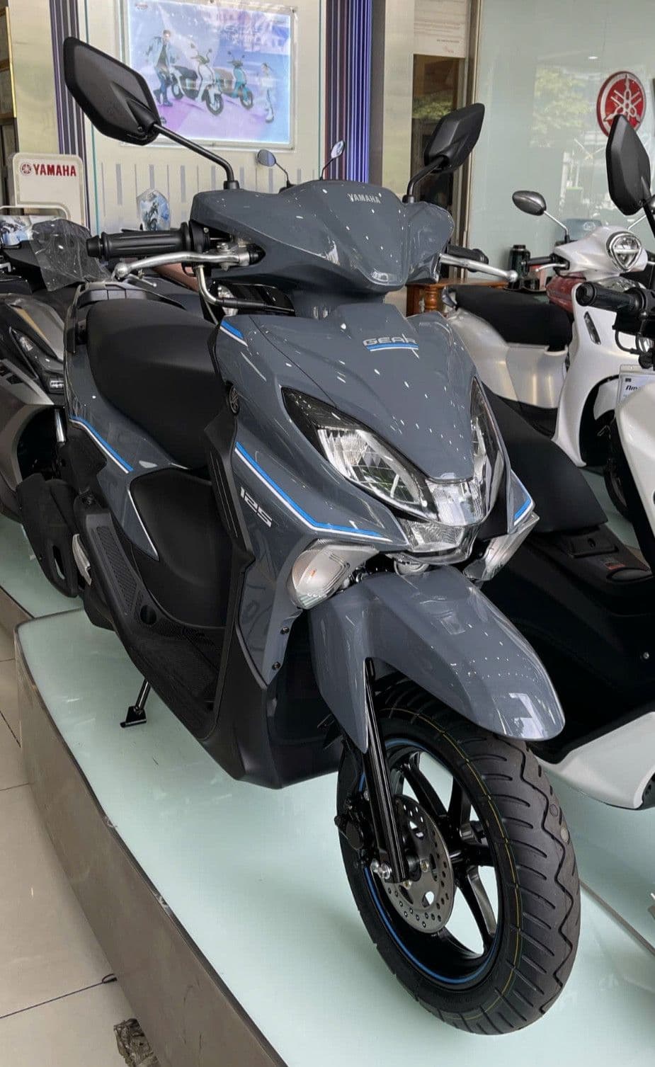 Một chiếc xe tay ga Yamaha Gear 125 Hybrid màu xám trong showroom, minh họa cho các giải pháp điện hóa và thân thiện môi trường trong ngành xe máy.