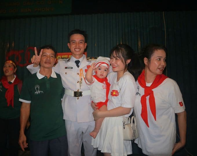 Một chiến sĩ diễu binh chụp ảnh cùng gia đình và em bé, thể hiện niềm tự hào và sự truyền nối giá trị lịch sử cho thế hệ tương lai.