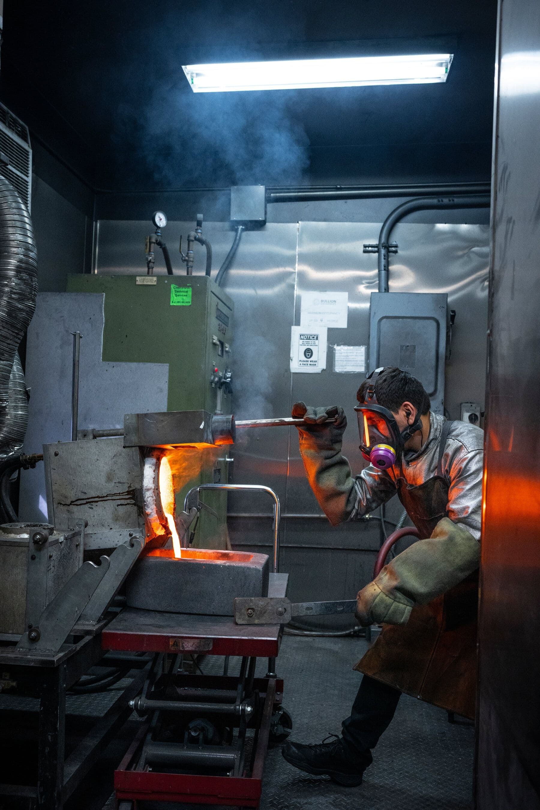 Một công nhân trong trang phục bảo hộ đang đổ vàng nóng chảy từ lò luyện vào khuôn, biến trang sức cũ thành kim loại thô.