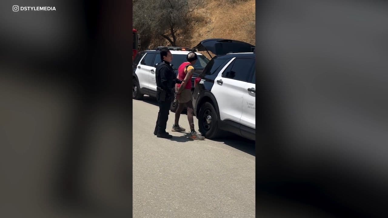 Một cảnh sát đang bắt giữ một người đàn ông bên cạnh xe cảnh sát, tượng trưng cho những điều bất ngờ và phức tạp trong cuộc sống đô thị ở California.