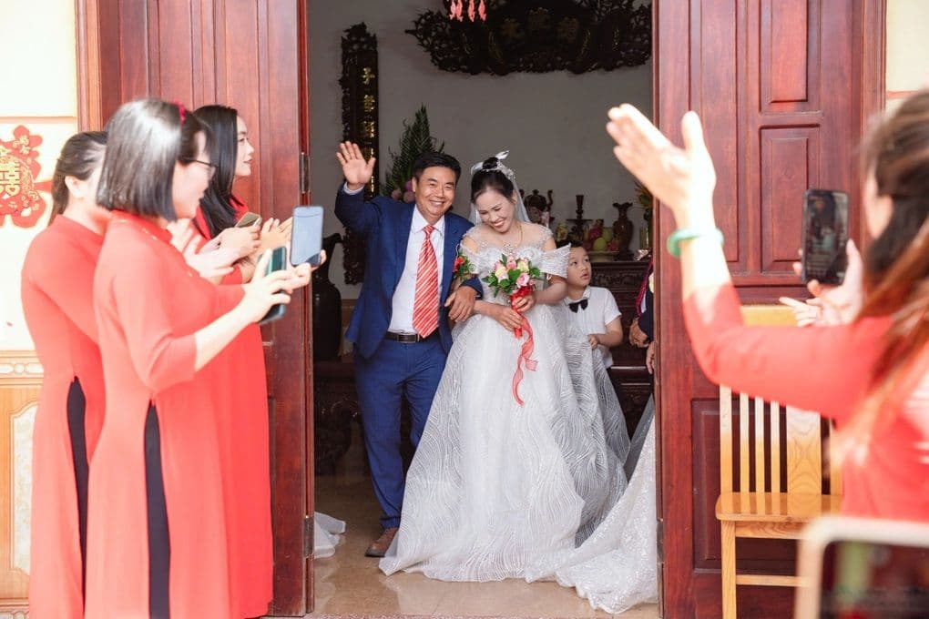 Một cặp đôi con cháu rạng rỡ vẫy tay chào khách mời trong hôn lễ tái hiện, thể hiện niềm hạnh phúc.