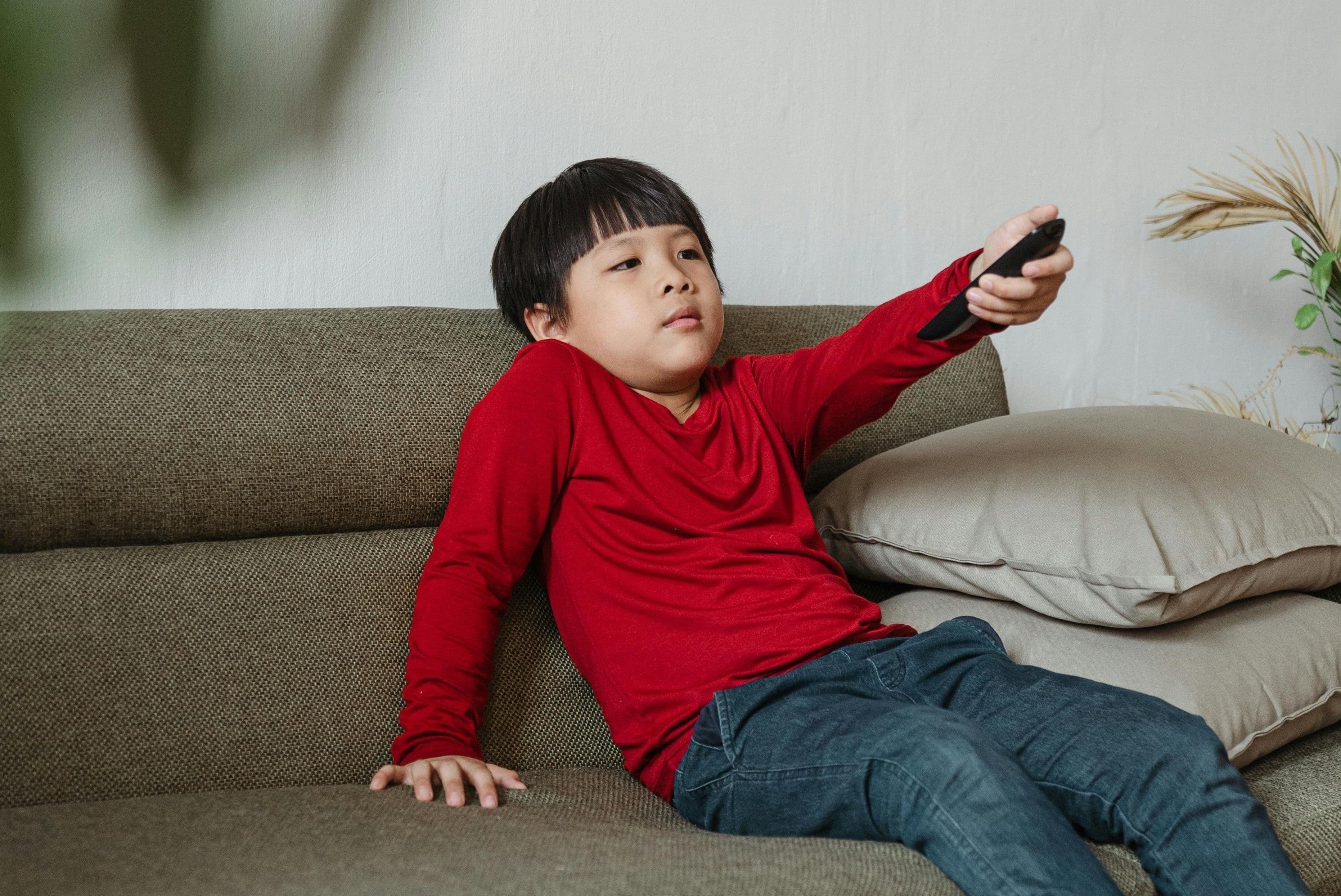 Một cậu bé thư giãn trên ghế sofa, xem TV trong kỳ nghỉ lễ, thể hiện sự thoải mái và tận hưởng thời gian rảnh rỗi.