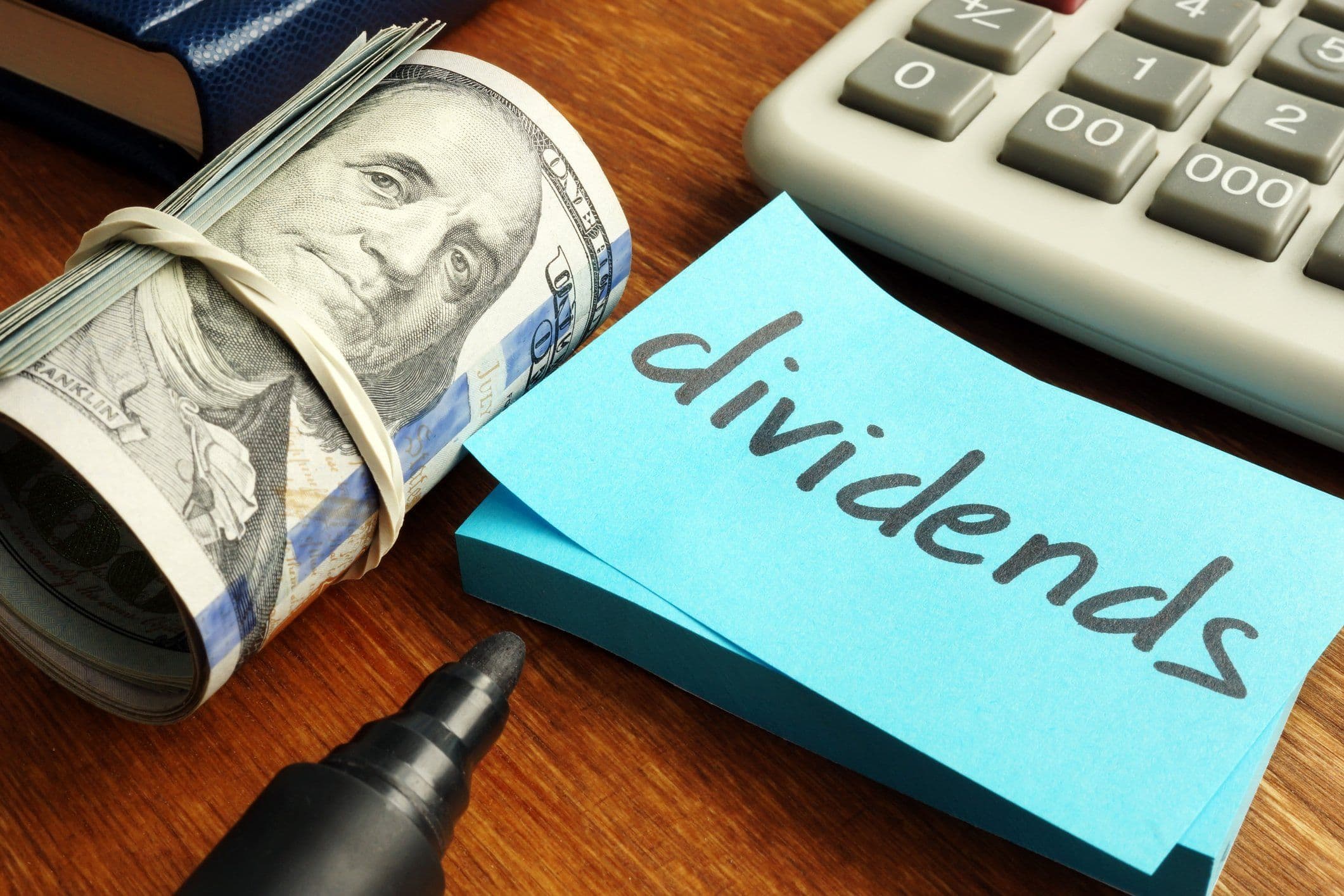 Một cuộn tiền đô la và giấy ghi chú 'dividends', tượng trưng cho lợi nhuận và chi phí trong đầu tư ETF.