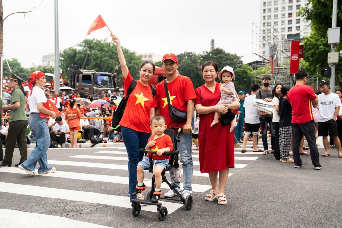 Một gia đình ba thế hệ mặc áo cờ đỏ sao vàng, đứng trên đường phố Hà Nội, một người giơ cao cờ Việt Nam.