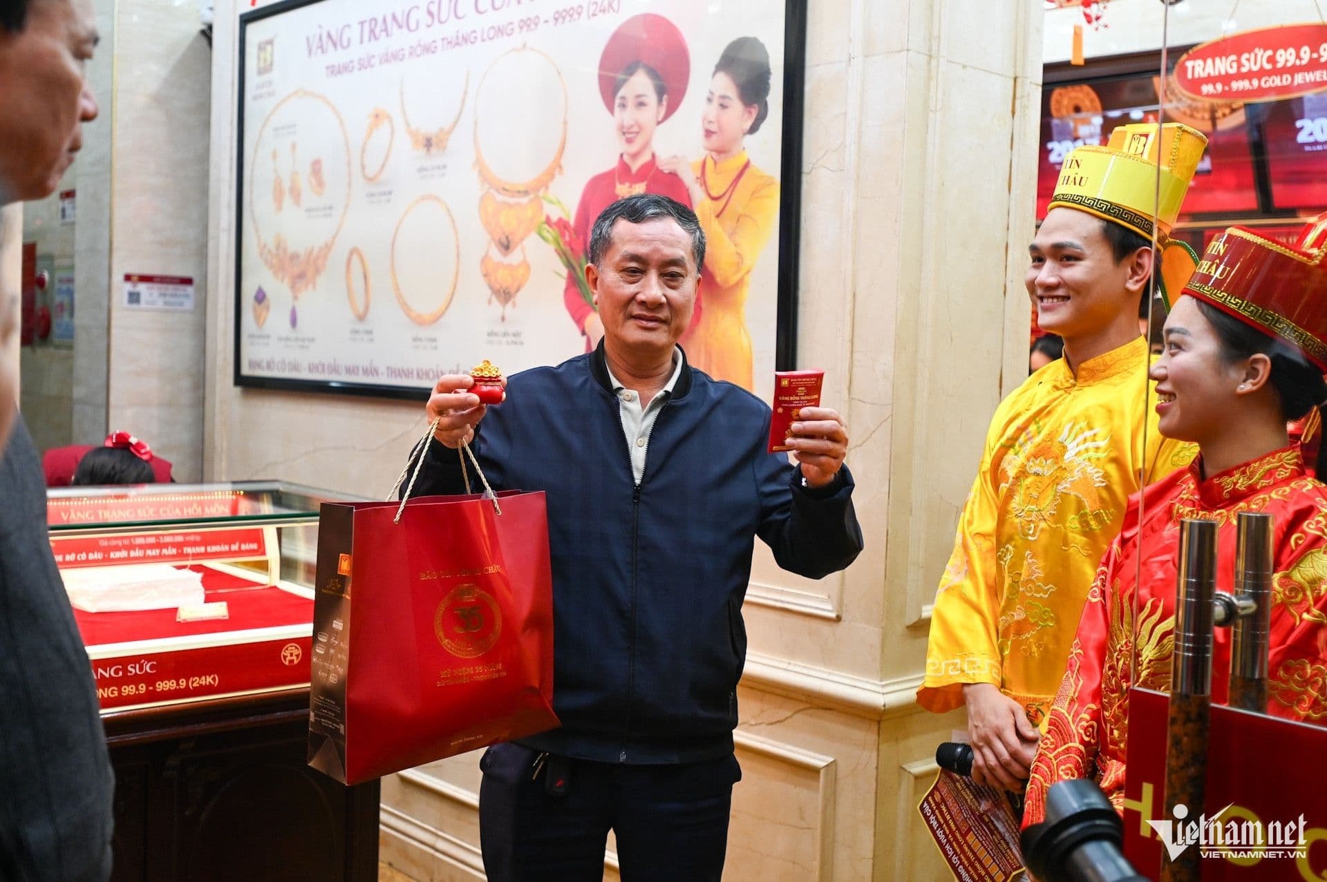 Một khách hàng vui vẻ nhận vàng và túi quà từ nhân viên mặc trang phục truyền thống, thể hiện niềm vui đón lộc đầu năm.