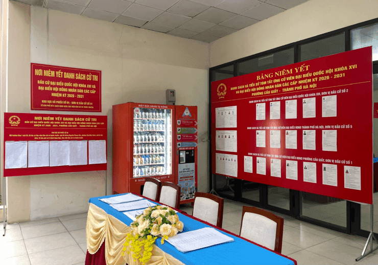 Một khu vực bỏ phiếu bầu cử với các bảng niêm yết danh sách cử tri và ứng cử viên, minh họa quá trình bầu cử tại Việt Nam.