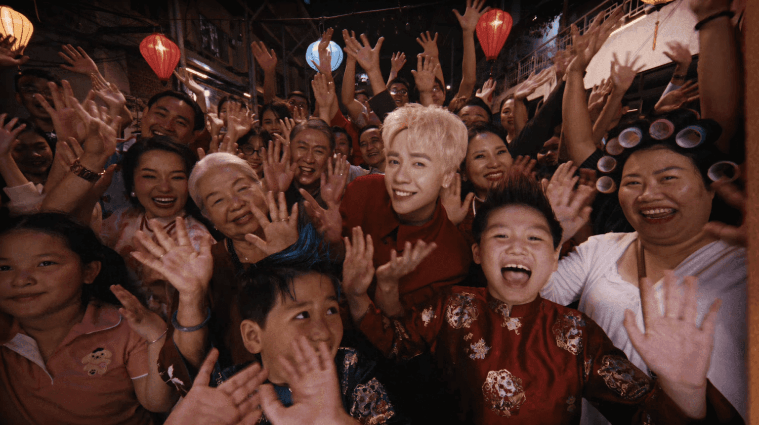 Một đám đông người Việt Nam, bao gồm trẻ em và người lớn, cùng một nghệ sĩ trẻ, đang vui vẻ vẫy tay trong không khí lễ hội, minh họa sức lan tỏa mạnh mẽ và khả năng tạo xu hướng của các MV Tết trên nền tảng số.