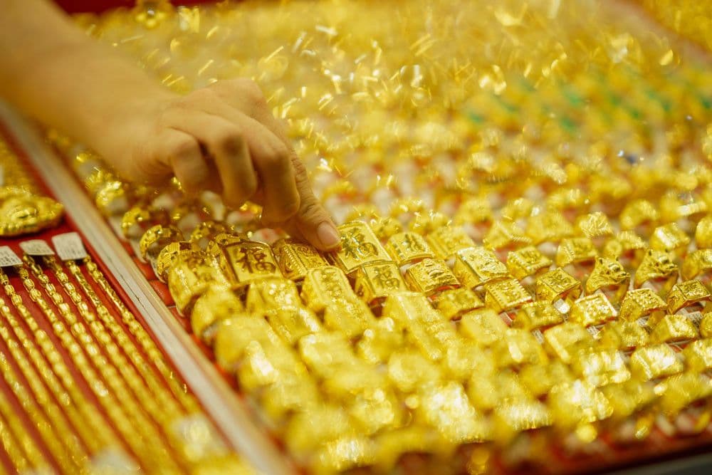 Một người đang chọn mua vàng miếng và nhẫn vàng, tượng trưng cho hoạt động giao dịch trên thị trường vàng.
