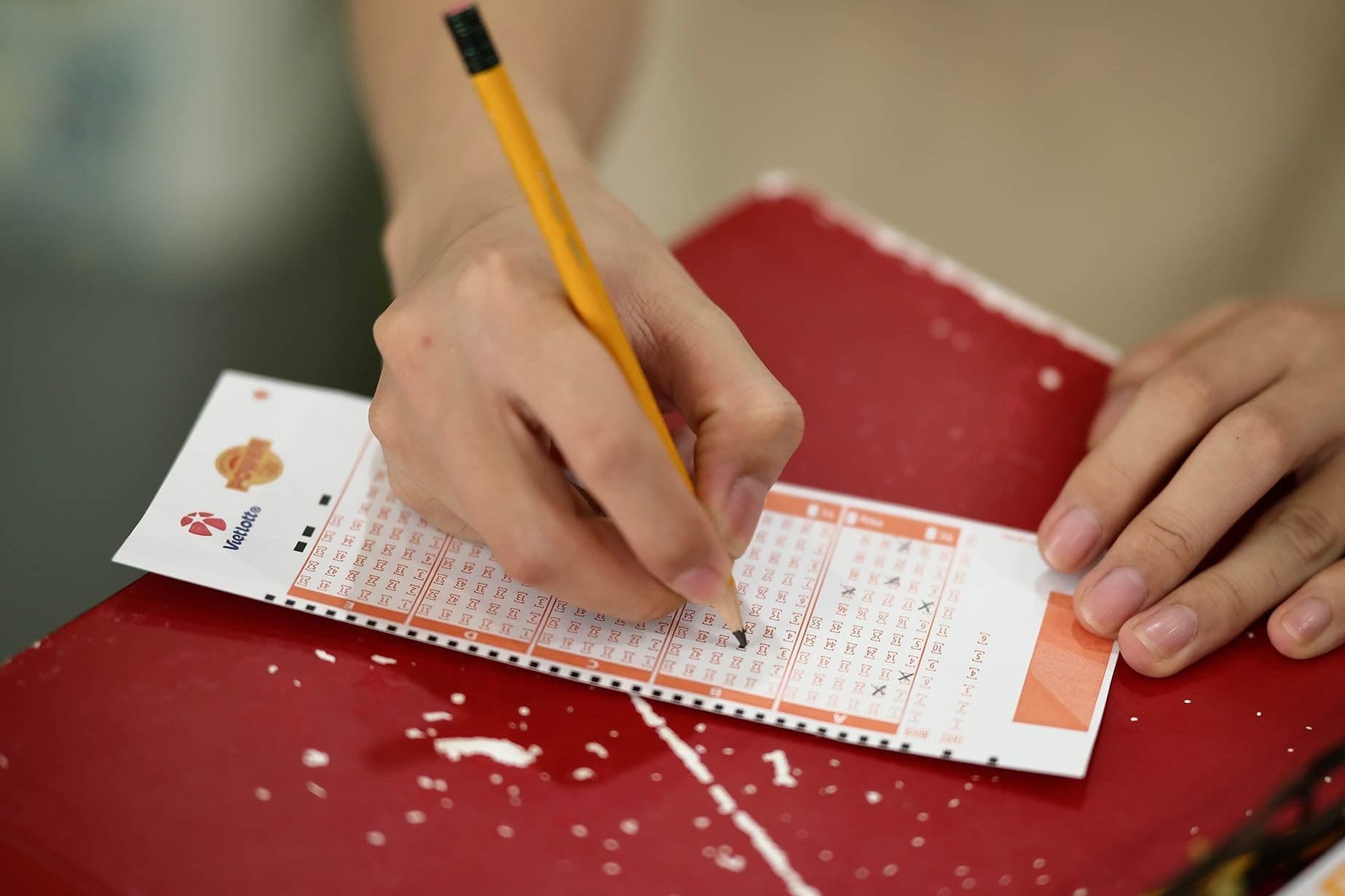 Một người đang dùng bút chì điền các con số vào tờ vé số Vietlott, thể hiện hành động tham gia xổ số.
