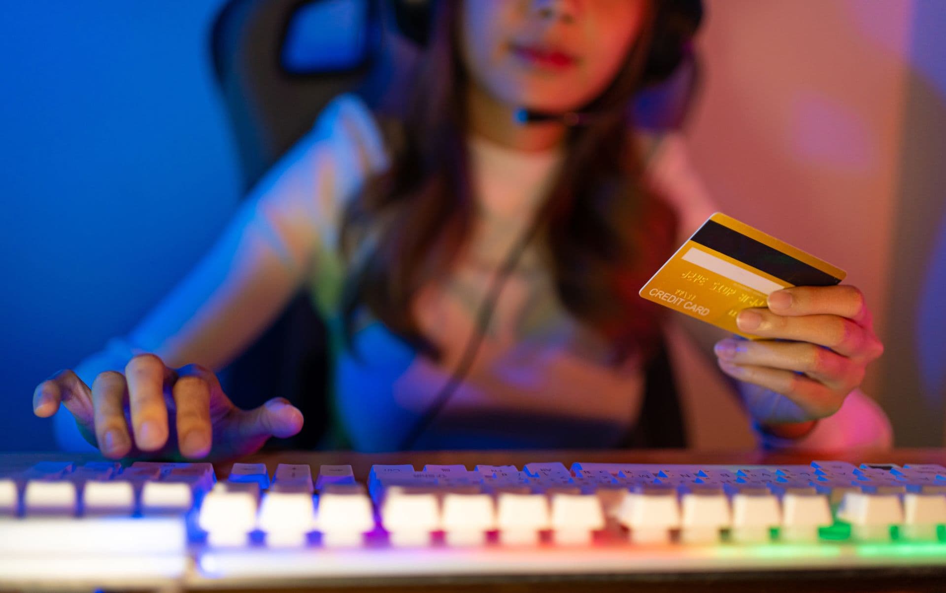 Một người chơi game đeo tai nghe đang tương tác với bàn phím và cầm thẻ tín dụng, thể hiện sự kết nối trực tiếp và hệ sinh thái tài chính trong livestream.