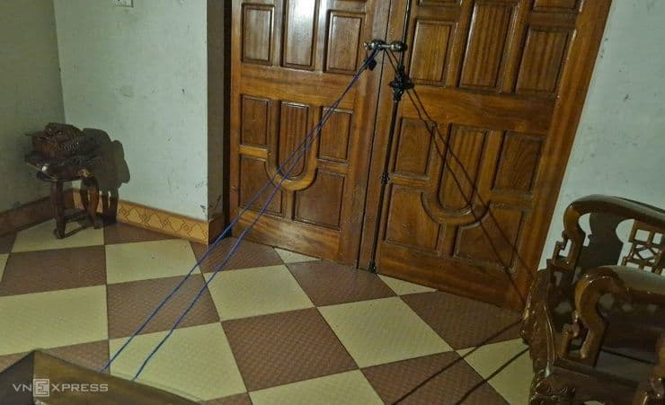 Một người dân đang chằng chống cửa nhà bằng dây dù để chống bão, thể hiện sự chủ động ứng phó và sức mạnh cộng đồng trong phòng thủ.