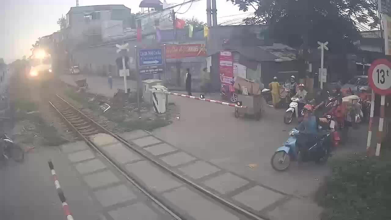 Một người đi xe máy cố tình vượt rào chắn đường sắt đã hạ khi tàu đang đến gần, minh họa nguy cơ tai nạn do ý thức kém.