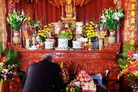 Một người đàn ông thành kính quỳ lạy trước bàn thờ gia tiên với mâm cúng trang trọng vào ngày mùng 1 âm lịch.