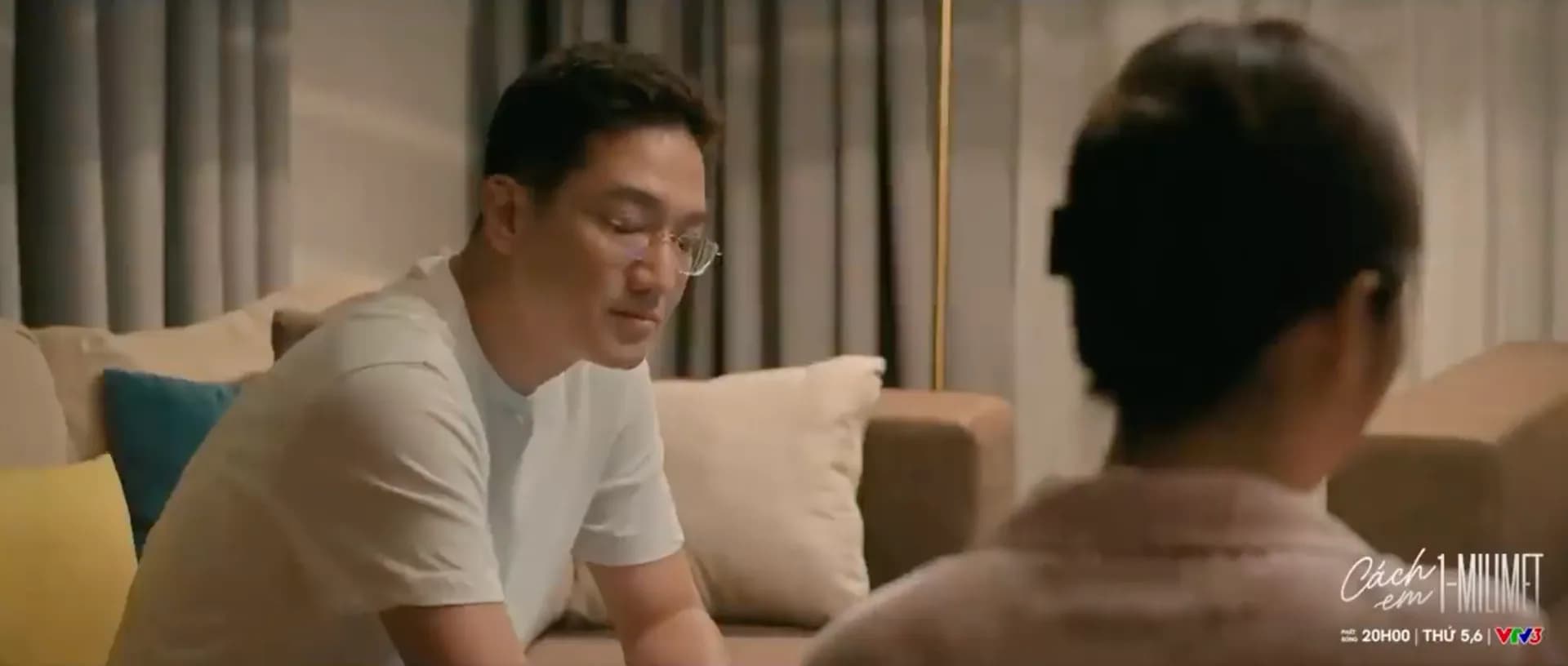 Một người đàn ông trưởng thành nhìn về phía một người phụ nữ, tượng trưng cho những khoảng cách cảm xúc và sự thay đổi theo thời gian trong phim 'Cách em 1 milimet'.