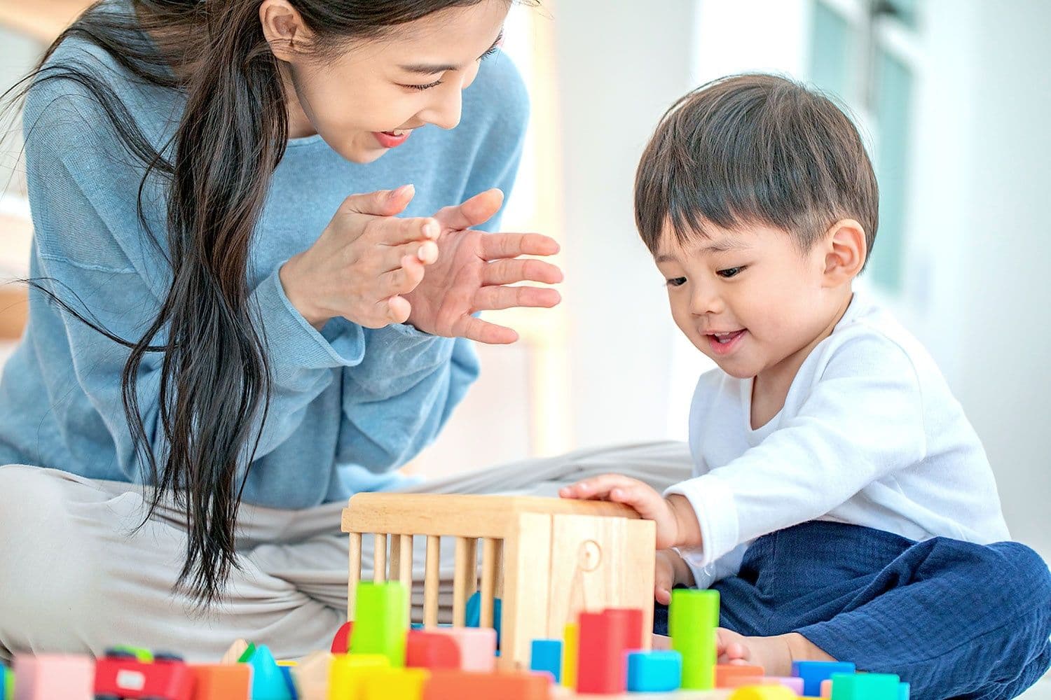 Một người phụ nữ đang chơi cùng một bé trai với khối đồ chơi, thể hiện sự chăm sóc và phục hồi tâm lý cho trẻ.